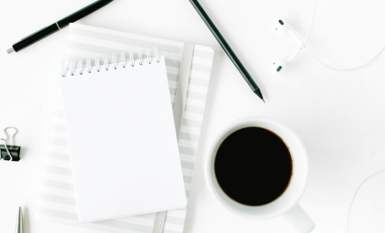a cup of coffee next to a black pen and a white notebook and a gray and white striped notebook