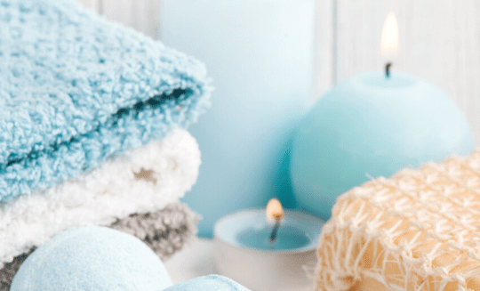 three folded towels in the color blue, white, and grey next to a white candle and a blue candle